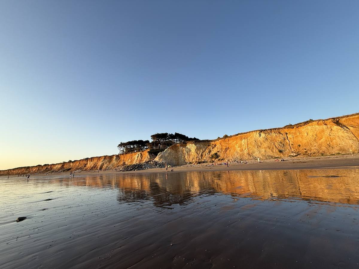Falaises dorées au soleil couchant, reflétées sur le sable mouillé
