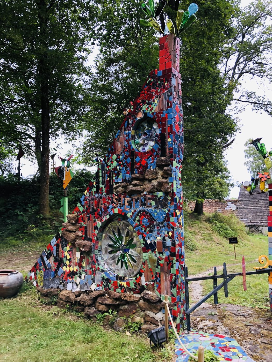 Deux rosaces percées dans une tour de céramique, encadrées de capsules et de fragments colorés.